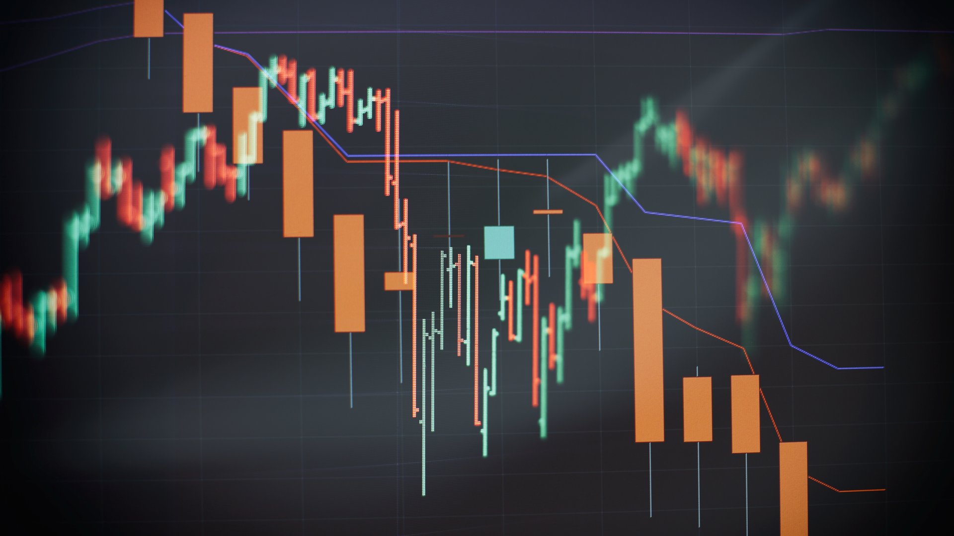 Close-up of a dark trading screen showing a glowing candlestick chart in orange and teal descending through a downtrend, with faint blue and red trend lines overlaid on a navy-black grid.